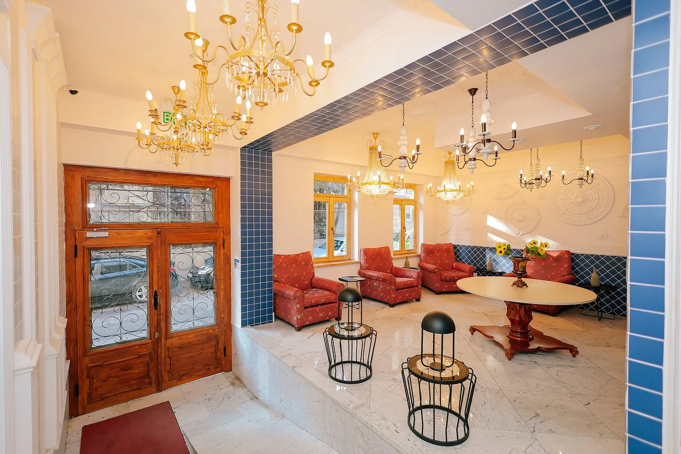 Magnolia's lobby: gold chandeliers, red floral armchairs, blue tiles and a round wooden table