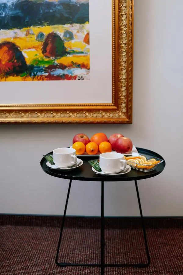 Tea, oranges and apples on a small black table under a gold-framed painting